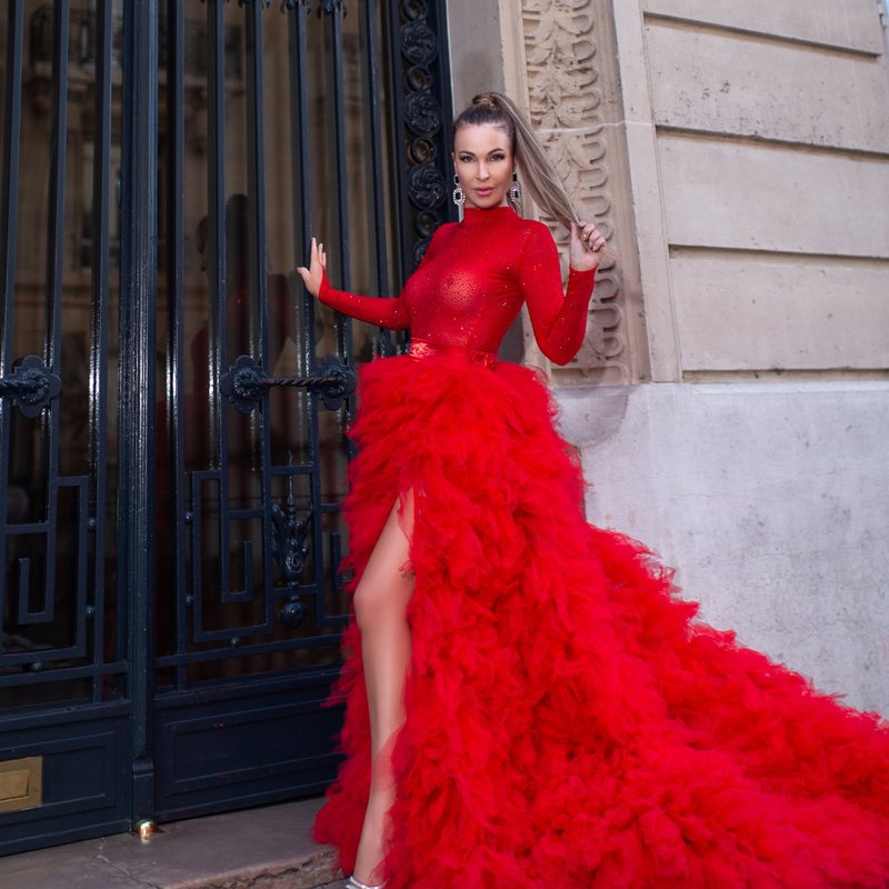 Woman in a red tulle gown with a long train by an ornate Parisian iron gate